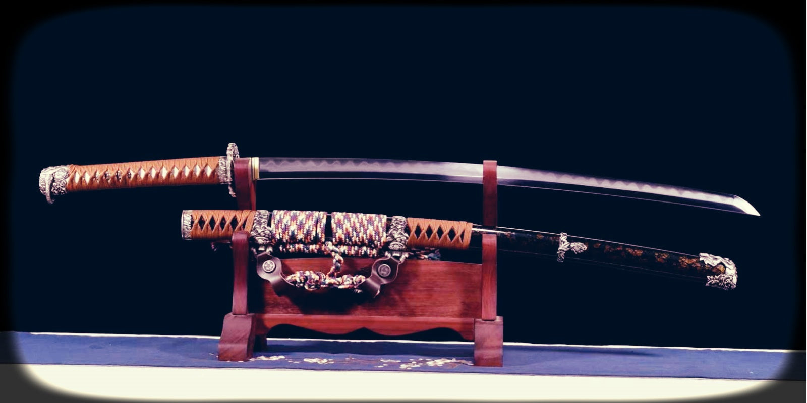 Functional samurai sword displayed with scabbard on a wooden stand, featuring a curved polished blade, wrapped handle, ornate fittings, and dark decorated saya.