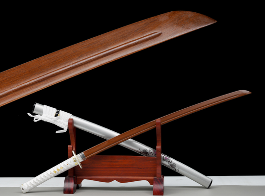 A wooden training sword displayed on a wooden stand, with a decorative silver scabbard in the background. A close-up of the blade’s fuller is shown above, highlighting its craftsmanship — ideal for beginner sword practice.